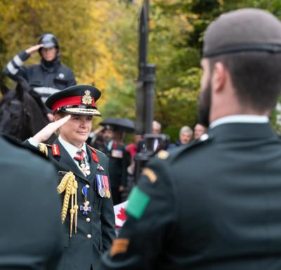 The Governor General Julie Payette, wearing an army uniform, salutes.  Servicemen and women stand in the foreground.
