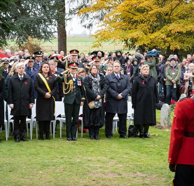 A large crowd stands in front of their chairs.  Governor General Julie Payette is standing center, in an army uniform, and salutes. 