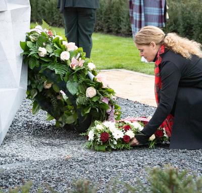 The Governor General kneels to place a wreath, decorated with flowers, at the base of a monument. 