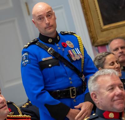 A recipient of the Order of Merit of the Police Forces stands before approaching the front of the room to accept his medal.