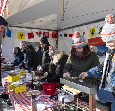 Half a dozen volunteers in winter gear serve raclette to visitors. 