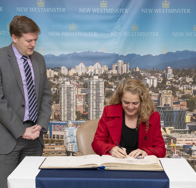 The Governor General signs the city`s guest book while the mayor stands beside her. 