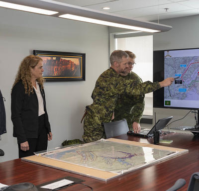 The Governor General is shown a map on a television screen of the floods. 