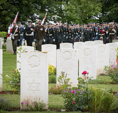 Rows of white tombstones in the Bény-sur-Mer Canadian War Cemetery to commemorate the 75th anniversary of D-Day. Military are aligned at a distance.