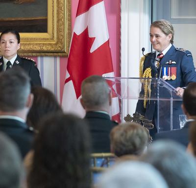 The Governor General delivers remarks at a podium, an aide-de-camp stands nearby.