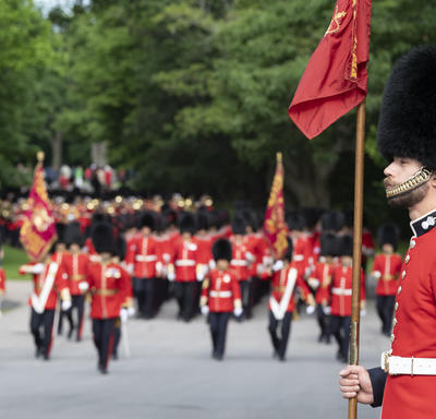 A guard stands at attention as the rest of the Ceremonial Guard make their way up the path towards Rideau Hall.