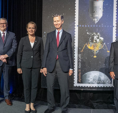 The Governor General poses for a photo on stage among executives next to the Apollo 11 stamps.