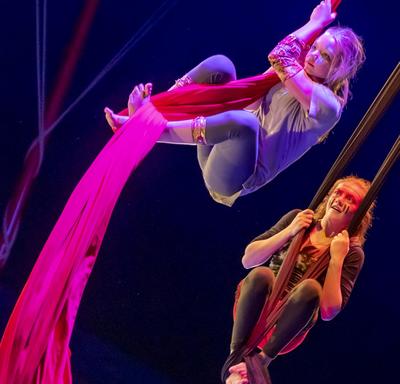 Two girls swing from silk acrobatic ropes. 