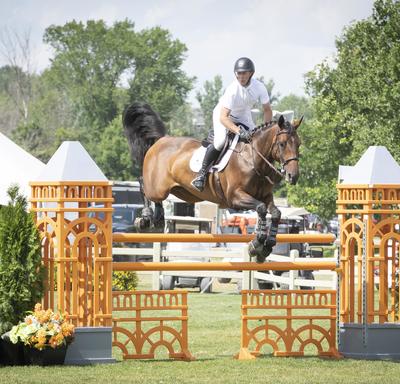 A rider and his horse jump over a fence during an outdoor equestrian competition.