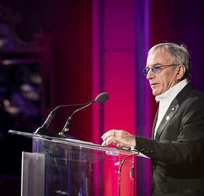 Right side view of Daniel Lamarre, President of Cirque du Soleil, speaking at a transparent podium.