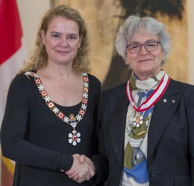 Louise Nadeau stands next to the Governor General.  Both smile at the camera.  They are wearing their Order of Canada insignia. 