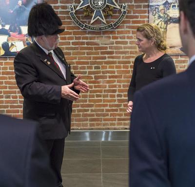 A men in a suit and wearing a black feathered hat talks to Governor General who listens attentively.