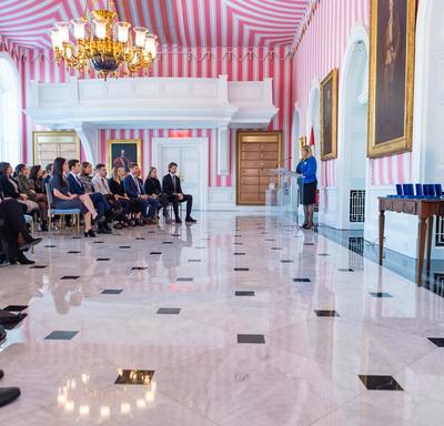Side view of Ms. Assunta Di Lorenzo speaking at a podium in front of an audience in Rideau Hall's red, black and white tent room.
