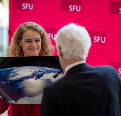 The Governor General presents the President of Simon Fraser University with a photo of Vancouver taken from space.