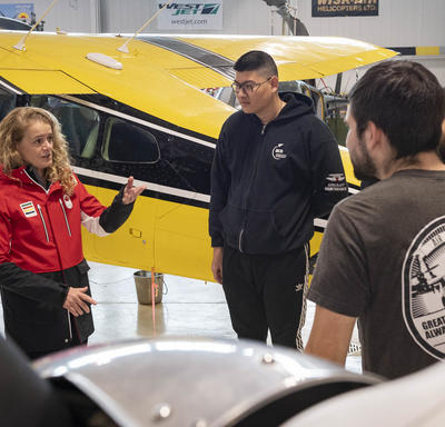 La gouverneure générale dans le hangar du Centre d'excellence en aviation avec des élèves, des enseignants et des avions.