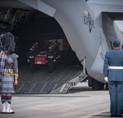 CAF members, including a bagpiper watch as a coffin, carried by CAF members, is taken off a plane.