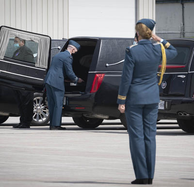 The Governor General salutes a coffin as it is placed in a hearse. 