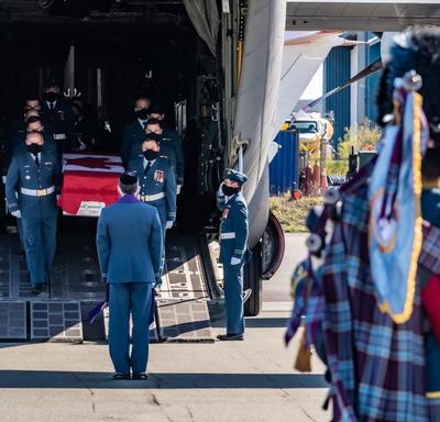 Captain Jennifer Casey’s coffin is carried off the plane by Canadian Armed Forces members. A bag pipe player is in the foreground of the picture. 