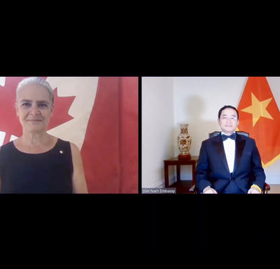 A computer screen split in two shows a woman on the left, standing in front of a Canadian flag. On the right, a man wearing a suit and bow tie is sitting in front of the flag of Vietnam.