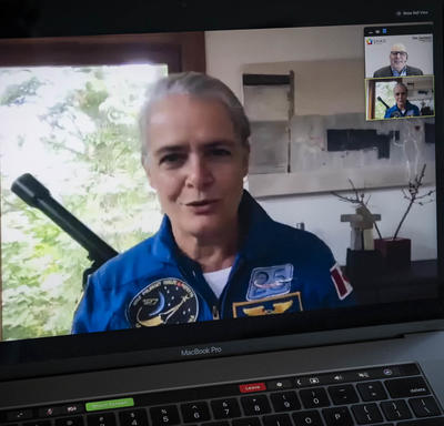 A woman in a blue space flight suit is shown on an open laptop screen.