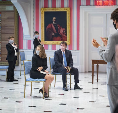 A man and a woman are seated while a small number of audience members applaud.