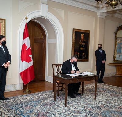 The Administrator and the Secretary looking on as a man signs a document.