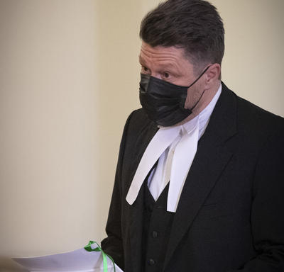 Un homme, portant une tenue noire avec un col blanc, tient des documents.