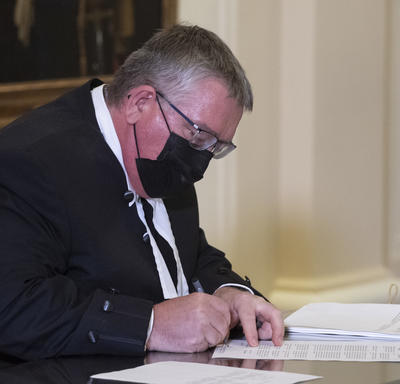 Un homme, assis à une table, signe un document.