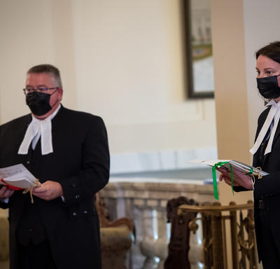 Two people, both dressed in black with white collars, each holding documents.