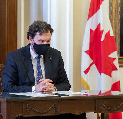 L’administrateur est assis à une table en train de lire un document. Un drapeau du Canada se trouve à l’arrière-plan.