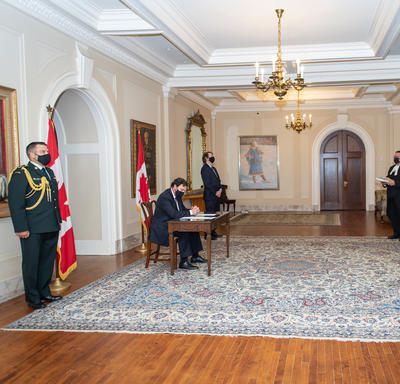 Quatre personnes se tiennent debout à une certaine distance pendant que l’administrateur, assis à une table, signe un document.