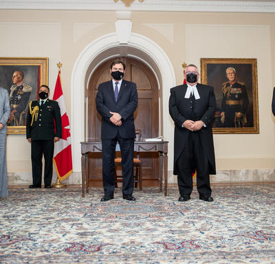 The Administrator is flanked on either side by two people. All five individuals wear masks and maintain physical distancing protocols.