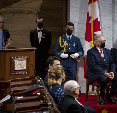 Le secrétaire du gouverneur général occupe le pupitre de la salle du Sénat. Mary Simon et son mari sont assis à sa gauche.