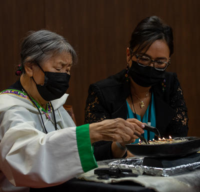 An Inuit Elder lighting the qulliq in the Senate. A woman is seated beside her. 