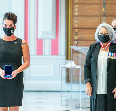 Une femme fraîchement décorée d’une médaille se tient près de la gouverneure générale Mary May Simon. Toutes deux portent un masque.