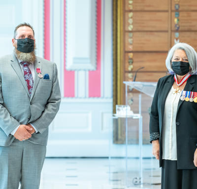 A man who has just been given a medal stands next to Governor General Mary May Simon. Both are wearing masks.