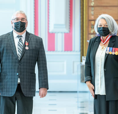 Un homme fraîchement décoré d’une médaille se tient près de la gouverneure générale Mary May Simon. Tous deux portent un masque.