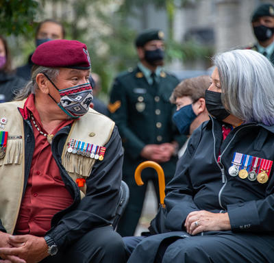 The Governor General speaks with a man seated to her right. Both wear masks.