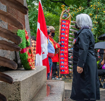 The Governor General lays a wreath at the base of the National Aboriginal Veterans Monument. Feathers are visible on the left side of the photo. 