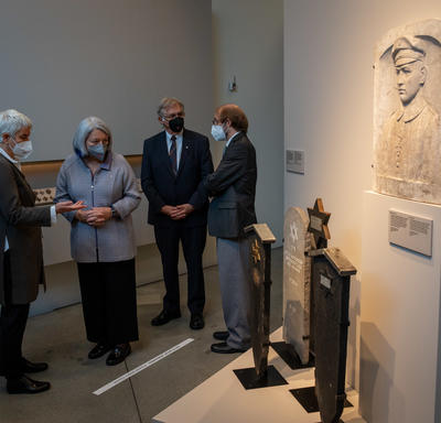 Their Excellencies are in a museum observing a piece of art. They are each speaking with someone respectively. 