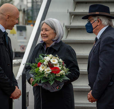 Governor General Mary May Simon, Mr. Whit Grant Fraser and Dr. Philipp Nimmermann are talking at the foot of a flight of stairs. Governor General May Simon is holding a bouquet.