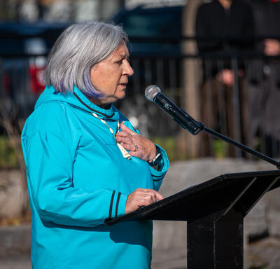 The Governor General addresses the crowd from the podium. She is wearing a blue parka pinned with a poppy.