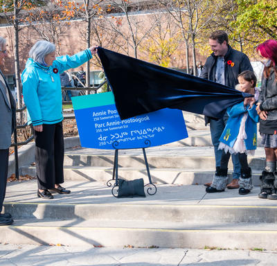The Governor General unveils a sign for the Annie Pootoogook Park. A man stands to her right. A small group stands on the other side of the sign.