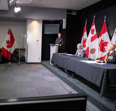 La gouverneure générale Mary Simon est assise à une longue table avec le général Wayne Eyre. Derrière eux, il y a des drapeaux canadiens et des Forces armées canadiennes.