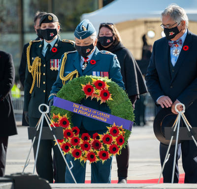The Governor General lays a wreath during the National Remembrance Day Ceremony. There are several people standing behind her, including Mr. Whit Fraser, Mrs. Josée Simard, and a woman wearing a military uniform.