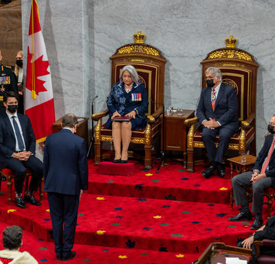 Their Excellencies seated at a pair of thrones. The Secretary to the Governor General stands before them.