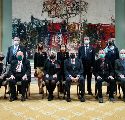 A group of eleven people, six sitting at the front and five standing behind, are posing for a photo in front of a large painting.