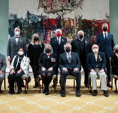 A group of eleven people, six sitting at the front and five standing behind, are posing for a photo in front of a large painting.