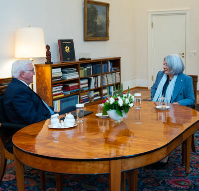 Le president de l’Allemagne Frank-Walter Steinmeier et la gouverneure générale Mary May Simon son assis autour d’une table de bois. Ils sont à six pieds l’un de l’autre. Ils parlent. Il y a des meubles le long du mur. 