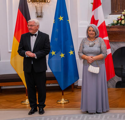 President Frank-Walter Steinmeier and Governor General Mary Simon are standing beside each other. There are three flags behind them: the flag of Germany, the European flag and the flag of Canada.